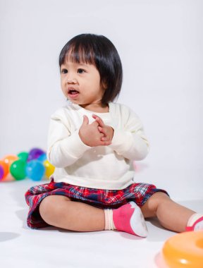 Küçük, şirin, kısa, siyah saçlı, Asyalı, ekoseli etekli, gülen, beyaz arka planda tek başına renkli yuvarlak toplarla oynayan küçük kız modelin stüdyo fotoğrafı..