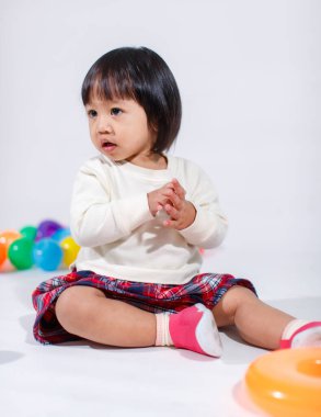 Küçük, şirin, kısa, siyah saçlı, Asyalı, ekoseli etekli, gülen, beyaz arka planda tek başına renkli yuvarlak toplarla oynayan küçük kız modelin stüdyo fotoğrafı..
