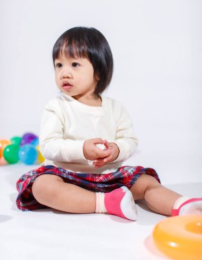 Küçük, şirin, kısa, siyah saçlı, Asyalı, ekoseli etekli, gülen, beyaz arka planda tek başına renkli yuvarlak toplarla oynayan küçük kız modelin stüdyo fotoğrafı..