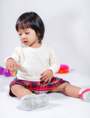 Küçük, şirin, kısa, siyah saçlı, Asyalı, ekoseli etekli, gülen, beyaz arka planda tek başına renkli yuvarlak toplarla oynayan küçük kız modelin stüdyo fotoğrafı..