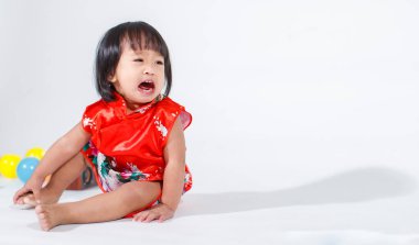 Kırmızı Çin Qipao kostümü giymiş, renkli plastik toplarla beyaz arka planda tek başına ağlayan Asyalı kız bebek modelinin stüdyo fotoğrafları..