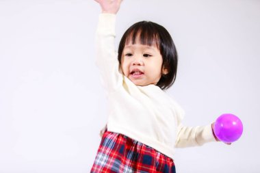 Küçük, şirin, siyah saçlı, Asyalı, ekoseli etekli ve gülümseyen beyaz arka planda tek başına renkli yuvarlak toplarla oynayan küçük bir kızın stüdyo fotoğrafı..