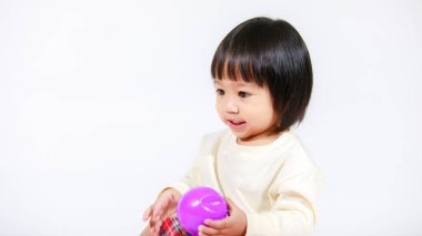 Küçük, şirin, kısa, siyah saçlı, Asyalı, ekoseli etekli, gülen, beyaz arka planda tek başına renkli yuvarlak toplarla oynayan küçük kız modelin stüdyo fotoğrafı..