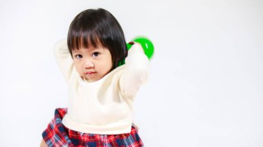 Küçük, şirin, kısa, siyah saçlı, Asyalı, ekoseli etekli, gülen, beyaz arka planda tek başına renkli yuvarlak toplarla oynayan küçük kız modelin stüdyo fotoğrafı..