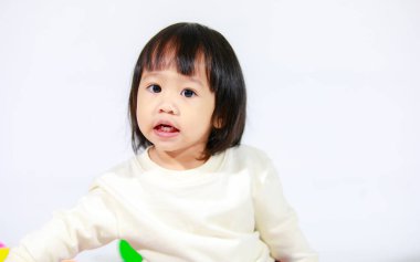 Küçük, şirin, kısa, siyah saçlı, Asyalı, ekose etekli, beyaz arka planda oturan ve gülümseyen kız çocuğunun stüdyo fotoğrafı.