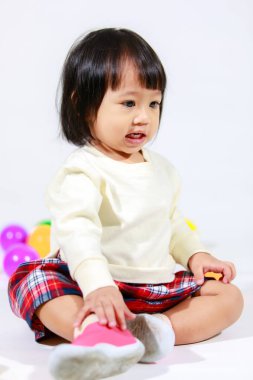 Küçük, şirin, kısa, siyah saçlı, Asyalı, ekoseli etekli, gülen, beyaz arka planda tek başına renkli yuvarlak toplarla oynayan küçük kız modelin stüdyo fotoğrafı..