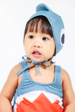 Beyaz arka planda oturan şirin gri köpek balığı kostümlü Asyalı küçük kız bebek modelinin stüdyo fotoğrafı.