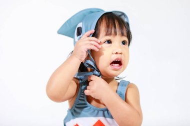 Beyaz arka planda oturan şirin gri köpek balığı kostümlü Asyalı küçük kız bebek modelinin stüdyo fotoğrafı.