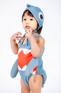 Beyaz arka planda duran şirin gri köpek balığı kostümlü Asyalı kız bebek modelinin stüdyo fotoğrafı.