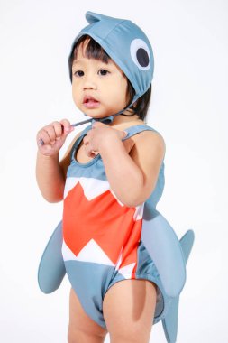 Beyaz arka planda duran şirin gri köpek balığı kostümlü Asyalı kız bebek modelinin stüdyo fotoğrafı.