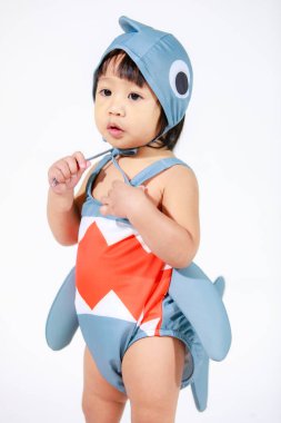 Beyaz arka planda duran şirin gri köpek balığı kostümlü Asyalı kız bebek modelinin stüdyo fotoğrafı.