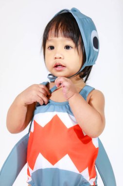 Beyaz arka planda duran şirin gri köpek balığı kostümlü Asyalı kız bebek modelinin stüdyo fotoğrafı.