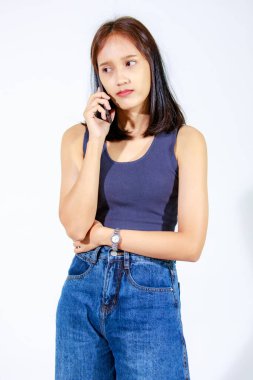 Asyalı genç kız modelin, beyaz arka planda akıllı telefon tutan bluz ve kotla izole edilmiş fotoğrafı.