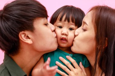 Mutlu Asyalı bir ailenin genç, mutlu bir eş ve kızının pembe arka planda kameraya gülümserkenki portresi. Anaokulu anaokulu çocuğu kız çocuğu babasının boynuna biniyor..