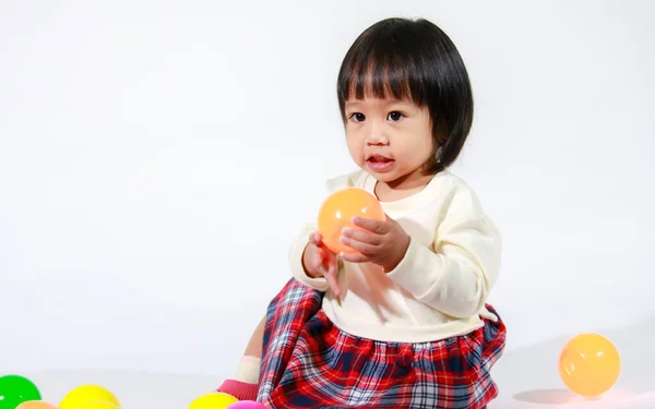 亚洲女婴穿着休闲格子裙坐在地板上笑着与五彩缤纷的圆形球衣在白色背景下独自玩耍的照片 — 图库照片