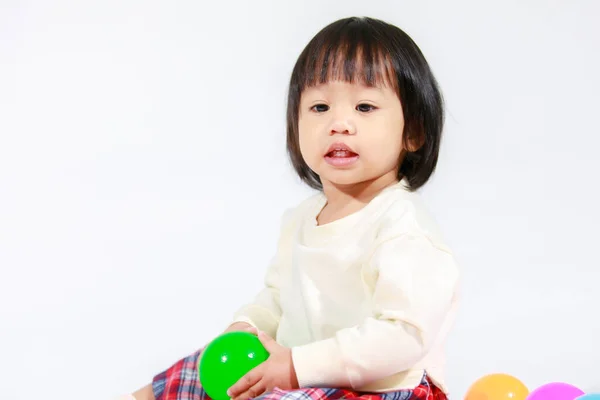 亚洲女婴穿着休闲格子裙坐在地板上笑着与五彩缤纷的圆形球衣在白色背景下独自玩耍的照片 — 图库照片