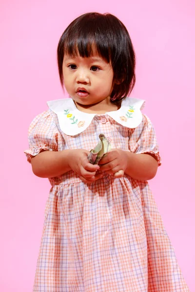 肖像工作室拍摄了可爱的亚洲幼稚园女模特儿 她穿着休闲装和鞋子 站在那里看着相机 手里拿着100美元钞票 背景是粉色的 — 图库照片