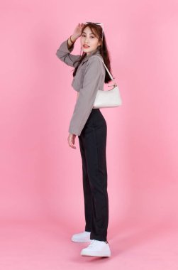 Asyalı modaya uygun yeniyetme kadın hippi modelinin portre çekimi. Üst sokak gündelik mahsul içinde. Ceket, güneş gözlüğü, çanta, pembe arka plan kamerasına bak..