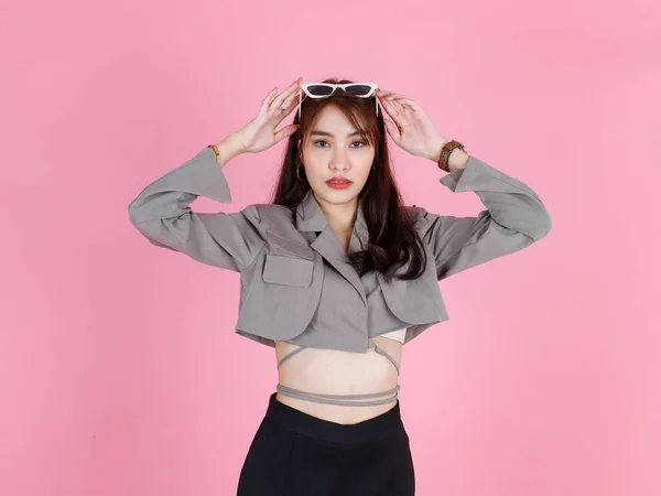 ポートレートスタジオショットのアジアの若い都市の流行の女性ヒップスターティーンエイジャーのファッションモデルでカジュアル作物トップストリート着用ジャケット保持サングラスで頭立って見て上のピンクの背景 — ストック写真