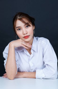 Asyalı genç, çekici, modaya uygun, beyaz gömlekli, makyajlı, siyah arka planda gülümseyen ve gülümseyen bir kadın modelin portresi..