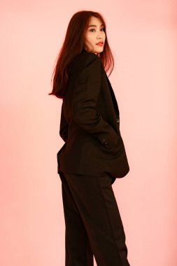 Asya 'nın güzel kentsel modayı, modern modaya uygun, siyah takım elbiseli, pembe arka plandaki kameraya bakarken çekilmiş bir portre resmi..