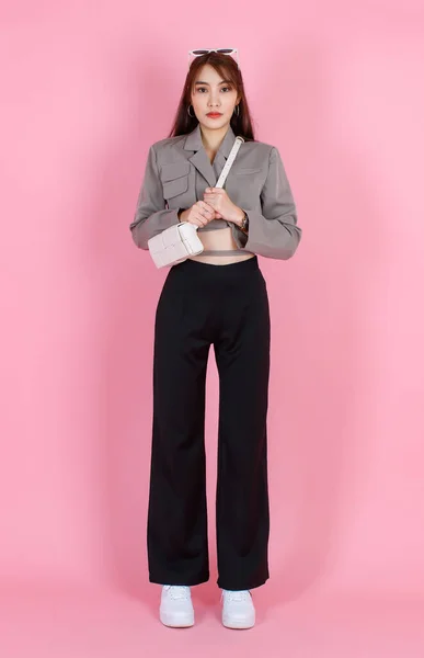 亚洲流行女嬉皮士少年模特儿穿着夹克衫太阳镜 头戴皮包 站在粉色背景的相机前拍照 — 图库照片