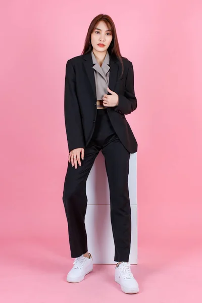 ポートレートスタジオショットのアジアの美しい都市トレンディーな現代的なファッショナブルな長い髪の女性ヒップスターティーンエイジャーモデルでカジュアルな黒スーツで作物トップシャツ座ってカメラでピンクの背景 — ストック写真
