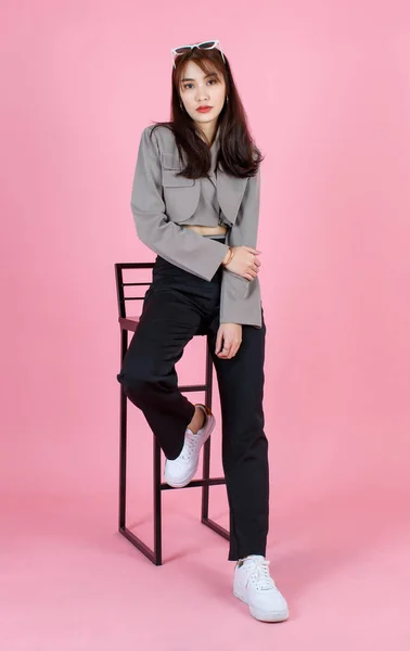 ポートレートスタジオショットのアジアの若い都市の流行の女性ヒップスターティーンファッションモデルでカジュアルな作物トップストリート着用ジャケット保持サングラス頭の上に座って見てカメラでピンクの背景 — ストック写真