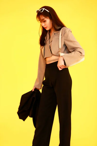 亚洲流行女嬉皮士少年模特儿穿着夹克衫太阳镜运动鞋手持手提包看着黄色背景的相机 — 图库照片