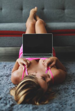 Beyaz, sarışın, seksi, pembe iç çamaşırlı manken kız. Halıya uzanmış, bacakları kanepeye koymuşlar. Elinde siyah, boş bir dizüstü bilgisayar varmış..