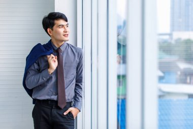 Milenyum Asyalı özgüvenli profesyonel erkek menajer, iş adamı resmi kıyafetli gülümseyen takım elbiseli adam gökdelen ofis penceresinin yanında dururken çekilmiş bir portre resmi.
