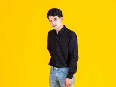 Asyalı genç adamın, profesyonel başarılı erkek iş adamının, sıradan siyah gömlekli, ayakta duran, sarı arka plandaki kameraya gülümseyen bir portresi.
