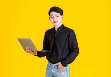 Asyalı mutlu erkek iş adamı resminin yakın plan portresi. Günlük kıyafetleri içinde. Sarı arka planda reklam için dizüstü bilgisayarı tutuyor.