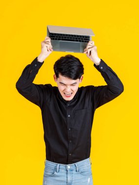 Bin yıllık Asyalı kızgın çılgın erkek iş adamı modelinin stüdyo fotoğrafı. Günlük kıyafet giymiş, elinde siyah boş dizüstü bilgisayarla sarı arka plandaki reklam metnini fırlatıyor..