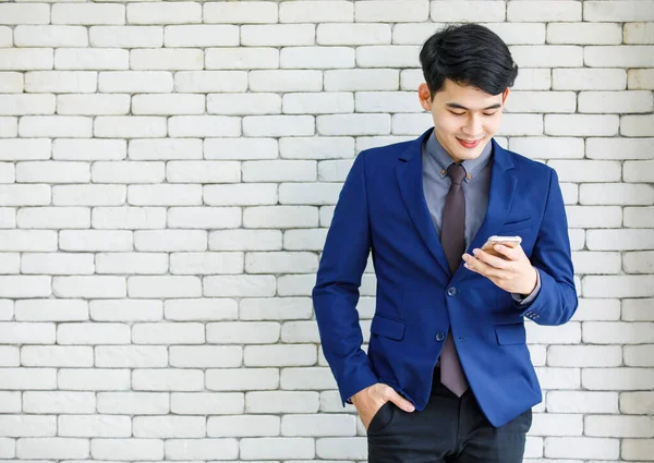 アジアのハンサムなプロの成功した男性実業家の肖像画のスタジオショットは 白いレンガの壁の背景に笑みを浮かべてスマートフォンを保持立って正式な青いスーツネクタイで起業家 — ストック写真