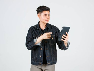 Portre stüdyosu Asyalı genç, kendine güvenen yakışıklı kısa saçlı, sıradan bir kot ceket giyen, elinde tablet bilgisayarla gri arka planda kameraya bakan hippi erkek modelini çekti..