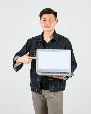 Asyalı yakışıklı erkek hippi modelin sıradan bir kot ceket giyip dizüstü bilgisayarı beyaz arka planda tutarken çekilmiş bir portre fotoğrafı.