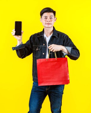 Sıradan kot ceketli Asyalı genç bir adamın portre çekimi. Kameraya bak. Boş siyah bir ekran akıllı telefon kullanıyor..