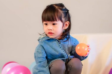 Küçük şirin anaokulu anaokulu kızı stüdyosu resmi. Günlük sokakta kot ceket giyer ve spor ayakkabı giyer. Elinde gri arka planda renkli plastik toplarla poz verir.