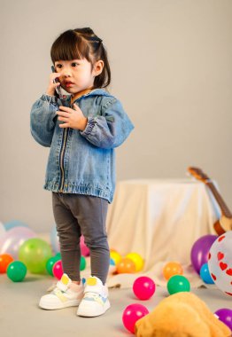 Küçük şirin, masum anaokulu anaokulu kızının resmi. Sıradan bir sokakta kot ceket giyiyor. Gri arka planda elinde akıllı telefonuyla kameraya bakıyor..