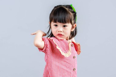 Küçük şirin anaokulu çocuğu, kırmızı uzun elbiseli, tek başına gülümseyen, gri arka planda renkli helyum hava partisi balonlarıyla oynayan kız çocuğunun portresi.