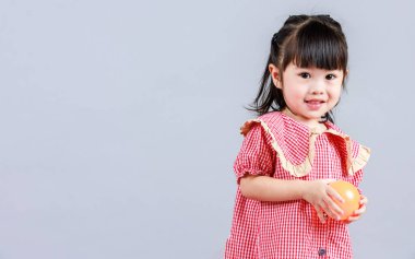 Küçük şirin anaokulu çocuğu, kırmızı uzun elbiseli, tek başına gülümseyen, gri arka planda renkli helyum hava partisi balonlarıyla oynayan kız çocuğunun portresi.