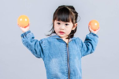 Stüdyoda, anaokulundaki küçük tatlı kız anaokulu çocuğunun tüm vücut fotoğrafları günlük sokakta kot ceket ve spor ayakkabıları giyer gri arka planda renkli plastik toplarla poz verir..