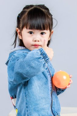 Stüdyoda, anaokulundaki küçük tatlı kız anaokulu çocuğunun tüm vücut fotoğrafları günlük sokakta kot ceket ve spor ayakkabıları giyer gri arka planda renkli plastik toplarla poz verir..