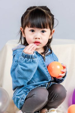 Küçük şirin anaokulu anaokulu kızı stüdyosu resmi. Günlük sokakta kot ceket giyer ve spor ayakkabı giyer. Elinde gri arka planda renkli plastik toplarla poz verir.