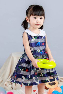 Küçük, masum anaokulu anaokulu kızı, mavi bir elbise giymiş, gri arka planda renkli balonlar tutan kameraya gülümseyen bir kızın portresi..