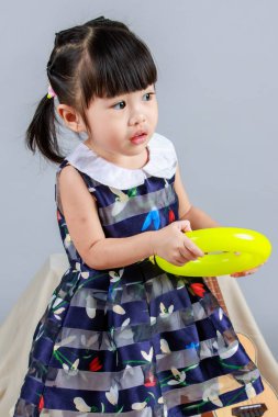 Küçük, masum anaokulu anaokulu kızı, mavi bir elbise giymiş, gri arka planda renkli balonlar tutan kameraya gülümseyen bir kızın portresi..