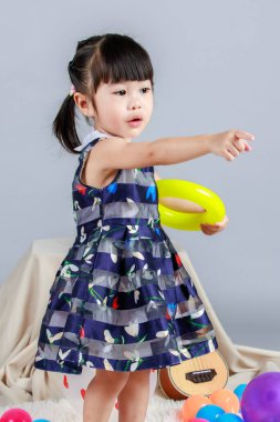 Küçük, masum anaokulu anaokulu kızı, mavi bir elbise giymiş, gri arka planda renkli balonlar tutan kameraya gülümseyen bir kızın portresi..