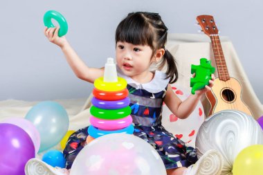 Renkli helyum balonları arasında oturmuş gri arka planda plastik halkalar ve dinozor oynayan küçük, masum anaokulu anaokulu kızı kızı fotoğrafı..