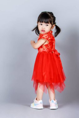 Geleneksel kırmızı Qipao Cheongsam elbisesi içindeki küçük, masum anaokulu anaokulu kızı Çin 'in yeni yılını gri arka planda kutluyor..